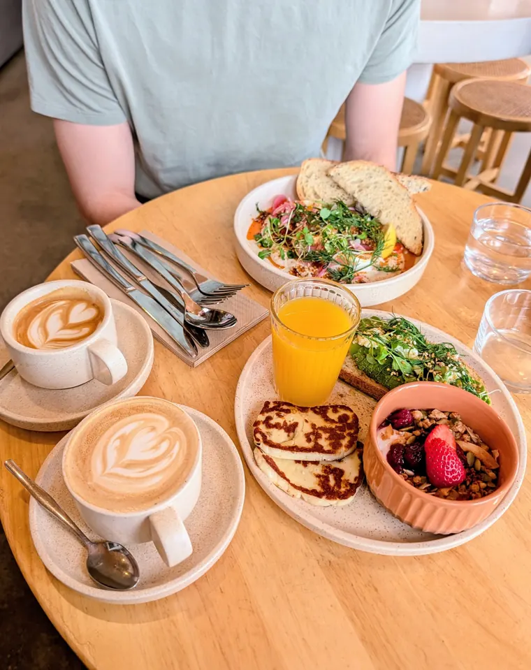 A brunch spread from above: lattes, juice, halloumi and a granola bowl